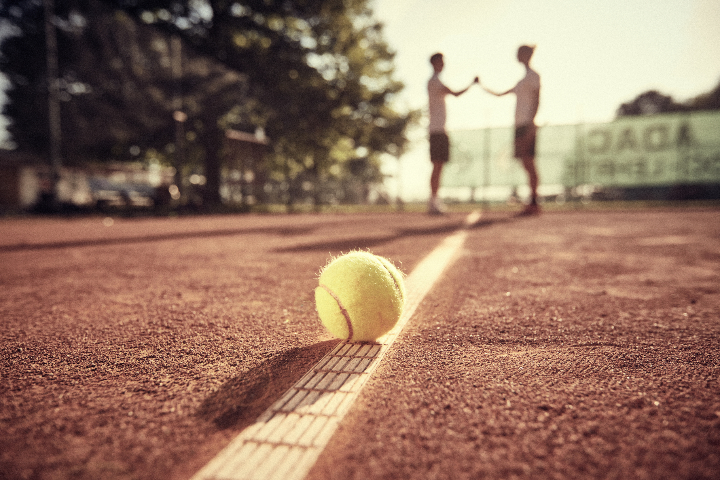 Tennisball auf Tennisplatz mit Trainer im Hintergrund
